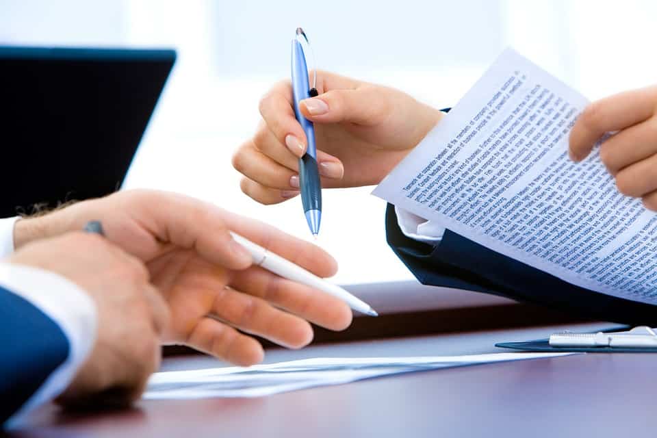 two persons holding pens and paper