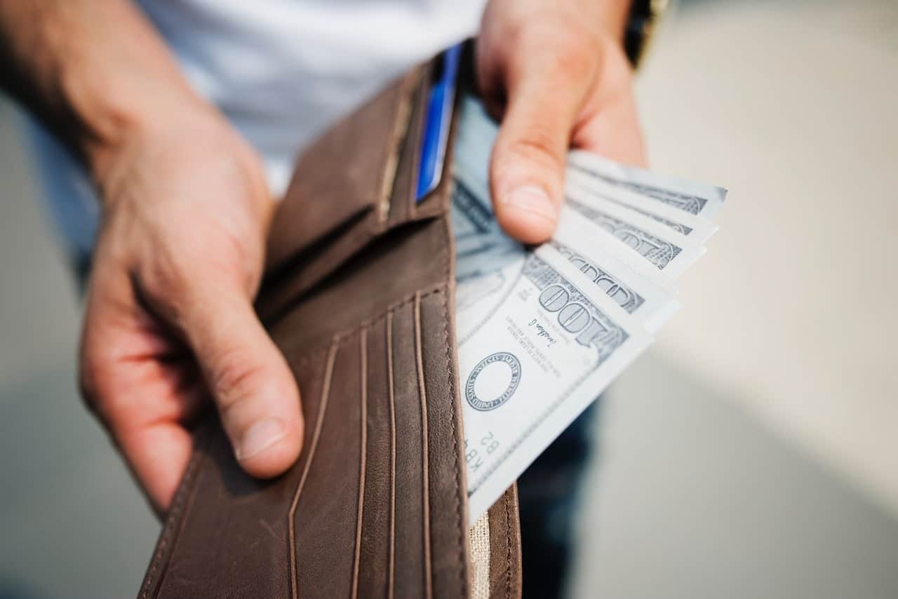 person holding brown wallet with cash