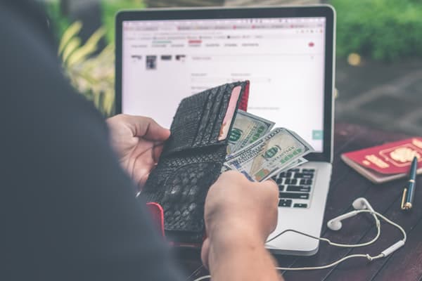 person holding money in front of computer